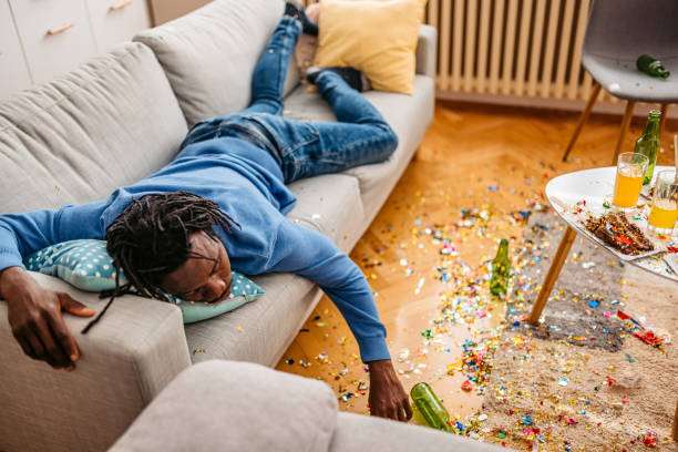 Young black man with hangover sleeping on the sofa in the living room and waking up after the birthday party the night before.